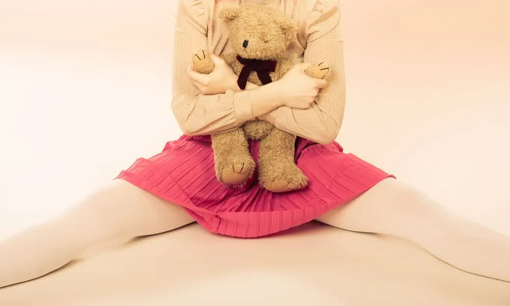 Người nữ mặc áo tay dài và váy xếp ly hai tay ôm gấu bông