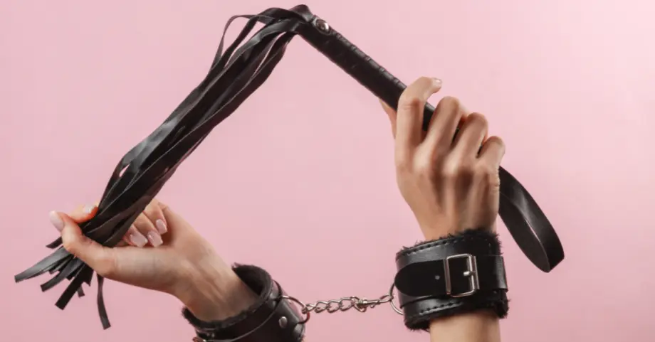 hai tay bị còng bởi còng lót lông cầm cây flogger