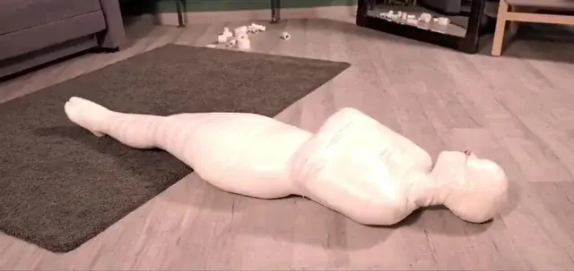 một người bị quấn băng toàn thân nằm trên sàn nhà