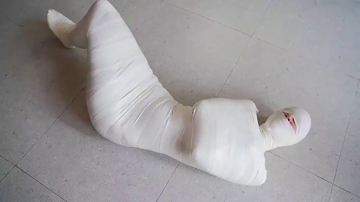 một người bị quấn băng gạc trắng nằm trên sàn