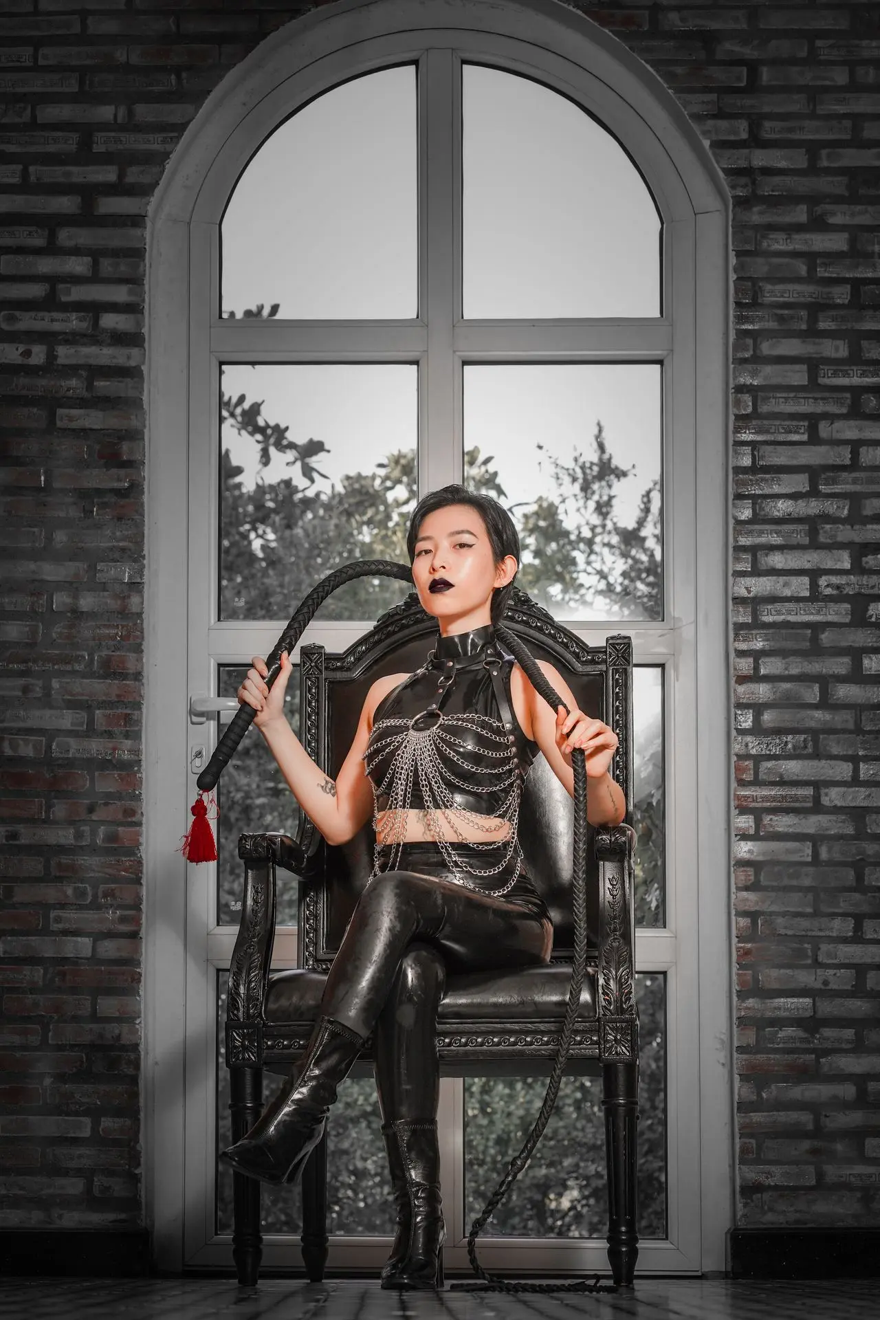 cô gái trong trang phục latex cầm roi ngồi trên ghế